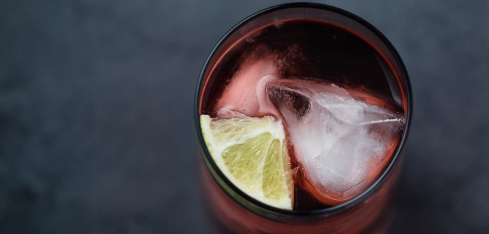 An above shot of a rum punch garnished with a lime wedge on a gray surface.